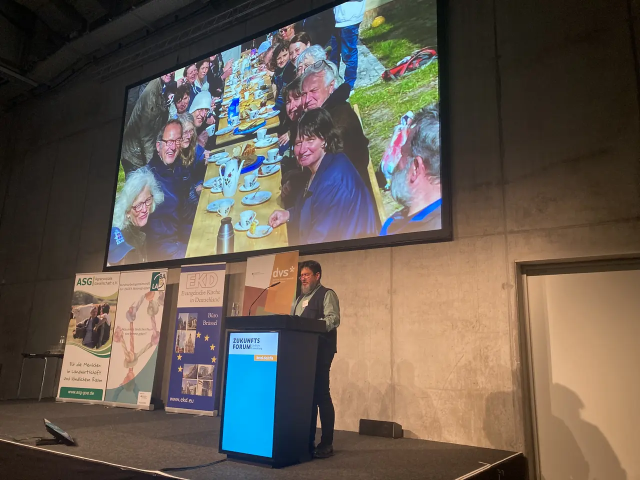 Man erkennt Pfarrer Schwieger von der NABU-Kirche Neu Temmen unter der Powerpoint-Präsentation mit einer Kaffetafel hinter dem Rednerpult im CityCube beim Zukunftsforum.